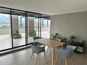 A modern indoor space with a wooden table and chairs, large windows, and potted plants.