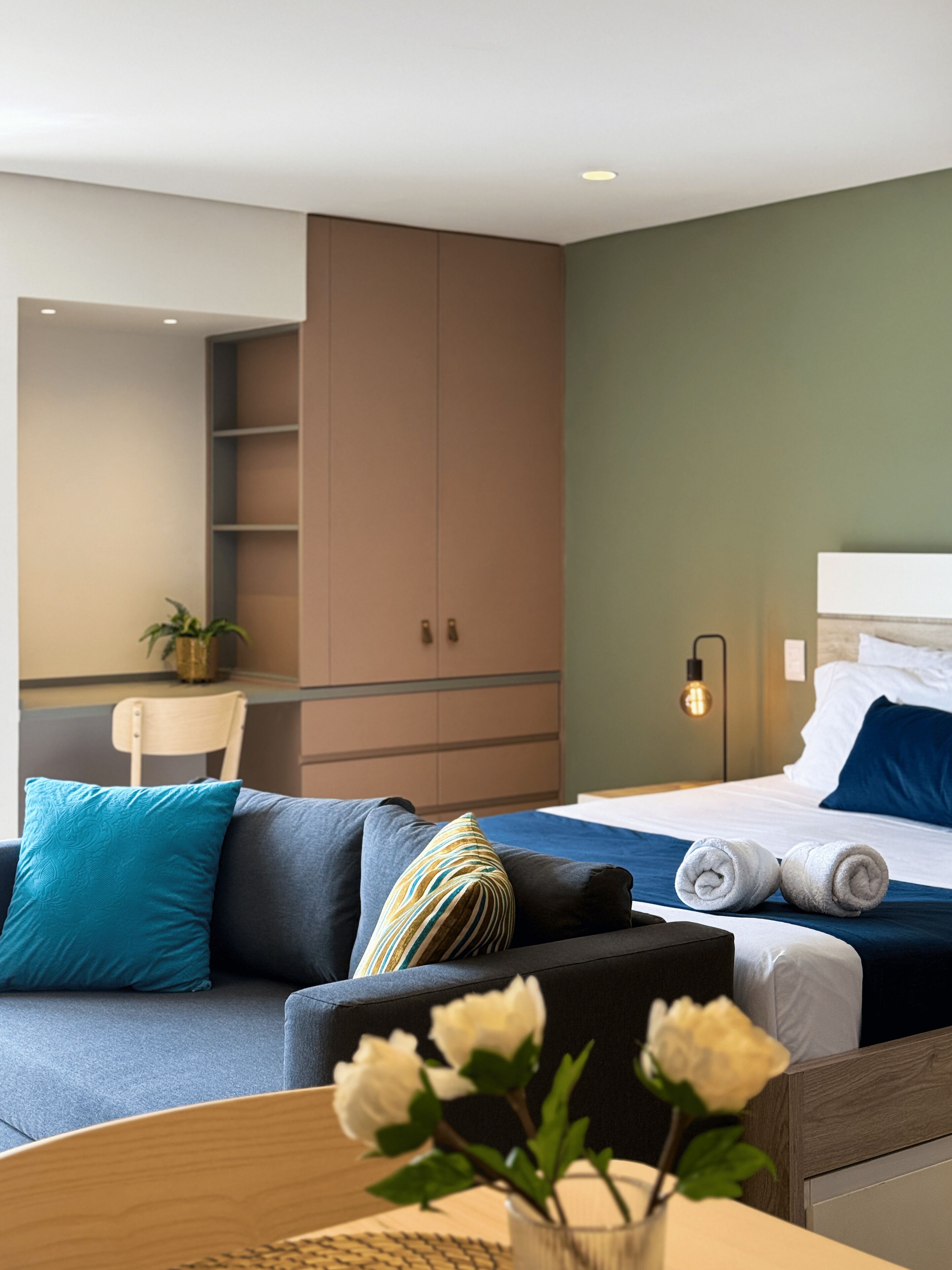 Una habitación de hotel moderna con cama, sofá, escritorio y una planta en maceta.
