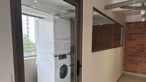 A laundry room with stacked washing machines and a dryer, a glass door, and a brick wall.