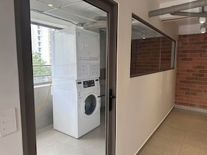 Uma lavanderia com máquinas de lavar empilhadas e uma secadora, uma porta de vidro e uma parede de tijolos.