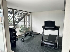 A gym with a treadmill, weights, and a stairwell.