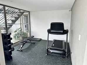 A small gym area with a treadmill, a bench, and dumbbells.