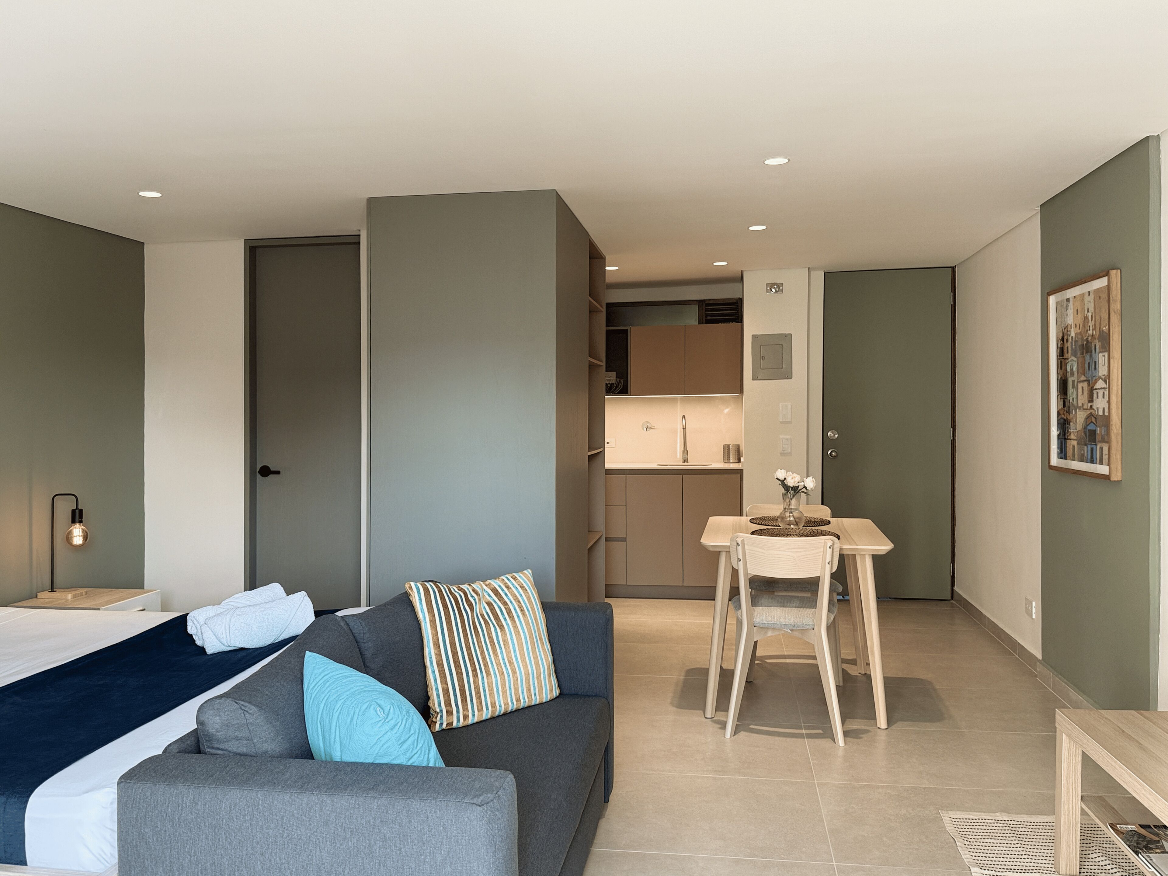 Ein modernes Hotelzimmer mit Bett, Sofa, kleinem Esstisch und Küchenzeile.
