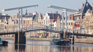 Eine Brücke über einem Fluss, im Hintergrund sind Gebäude zu sehen.