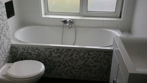 Ein Badezimmer mit einer weißen Badewanne, einer Toilette und einem Fenster über der Wanne.