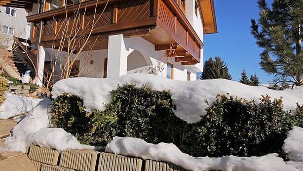 Un immeuble à plusieurs étages doté d’un balcon en bois et entouré d’un paysage enneigé.