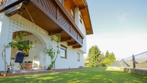 Une maison à deux étages avec un balcon en bois, une façade blanche et une pelouse bien entretenue.