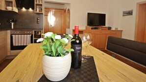 Une cuisine moderne avec des meubles en bois, une table à manger agrémentée d’un vase blanc et d’une bouteille de vin, et un téléviseur en arrière-plan.