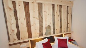 Une chambre d’hôtel avec un lit, deux oreillers rouges, une tête de lit en bois et une table de chevet sur laquelle se trouve un objet rouge.