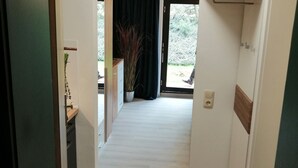 A hallway with a wooden floor, a door on the left, and a window with a curtain on the right. - Mike's apartment incl. Oberstaufen Plus Card (Steibis)