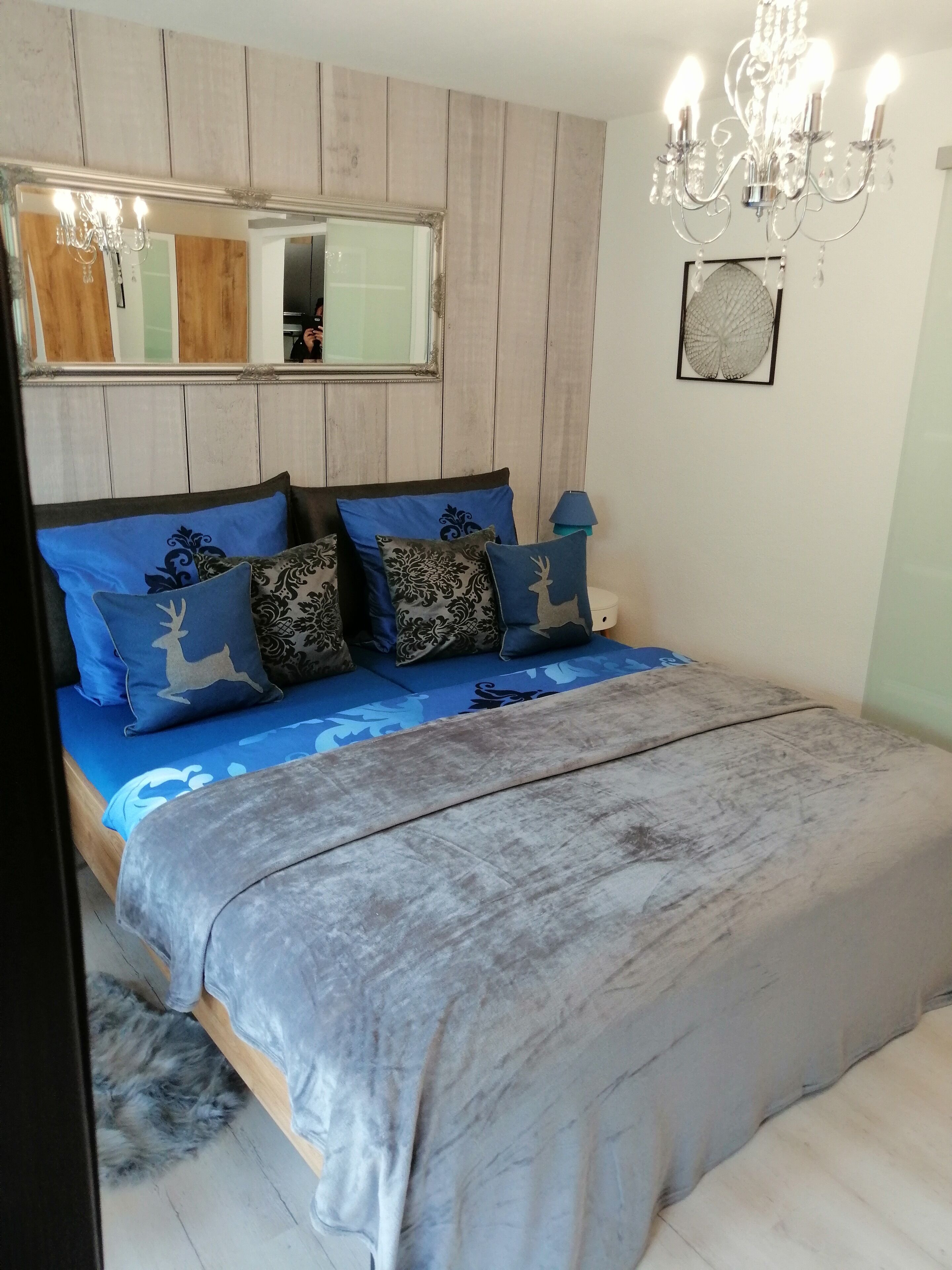 A bedroom with a bed, a mirror, a chandelier, and a framed artwork on the wall.