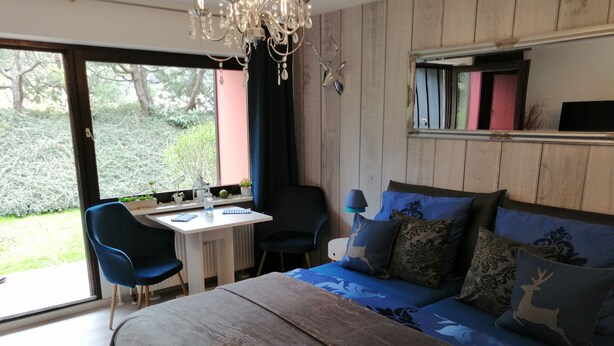 A bedroom with a bed, two chairs, a desk, and a window with a view of greenery. - Mike's apartment incl. Oberstaufen Plus Card (Steibis)