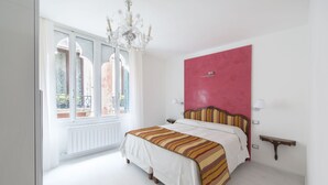 Quarto com uma cama grande, uma parede de destaque vermelha, um candelabro e uma janela com vista.