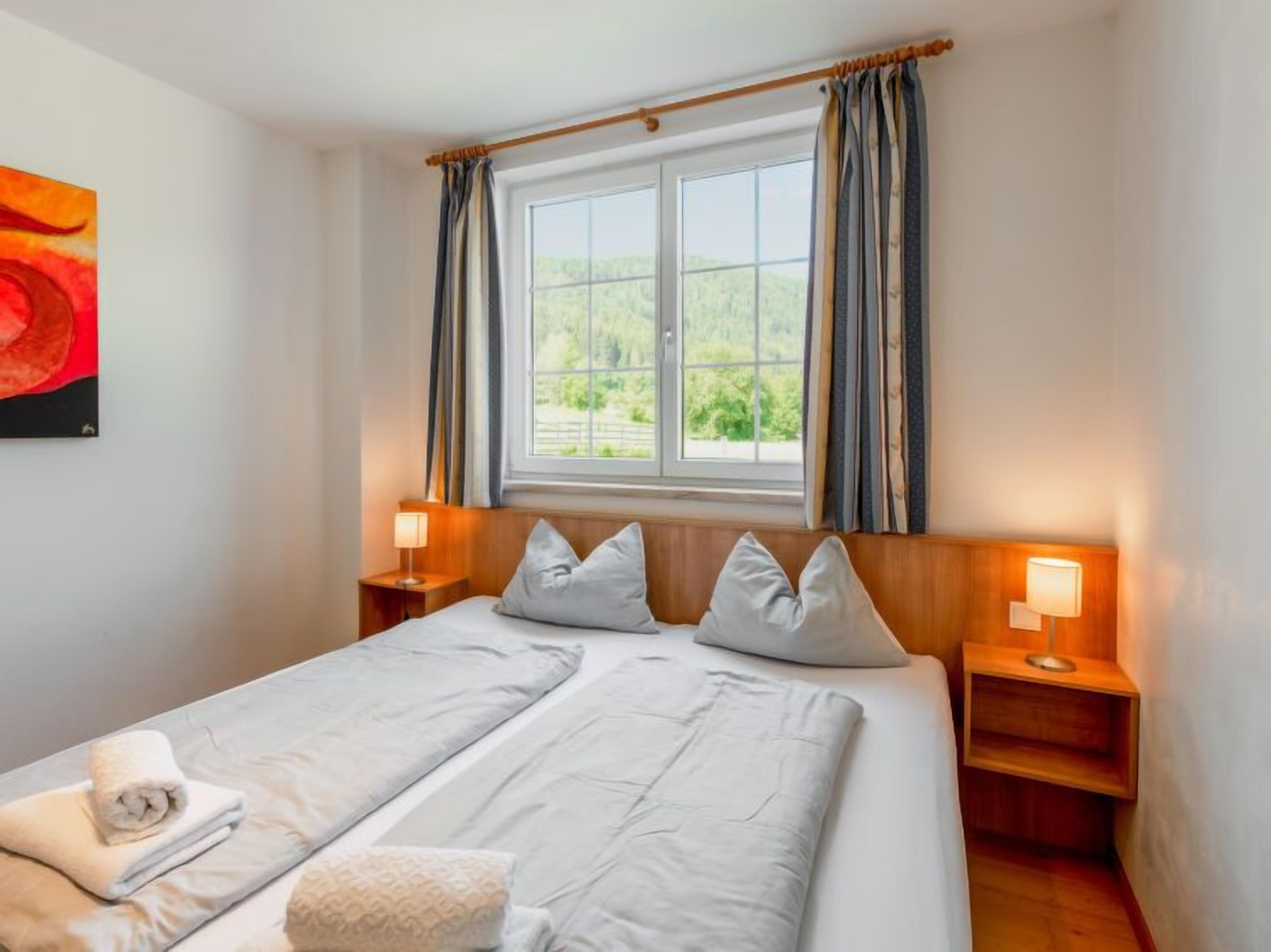 Een hotelkamer met een groot bed, twee nachtkastjes met lampen, een raam met gordijnen en een schilderij aan de muur.