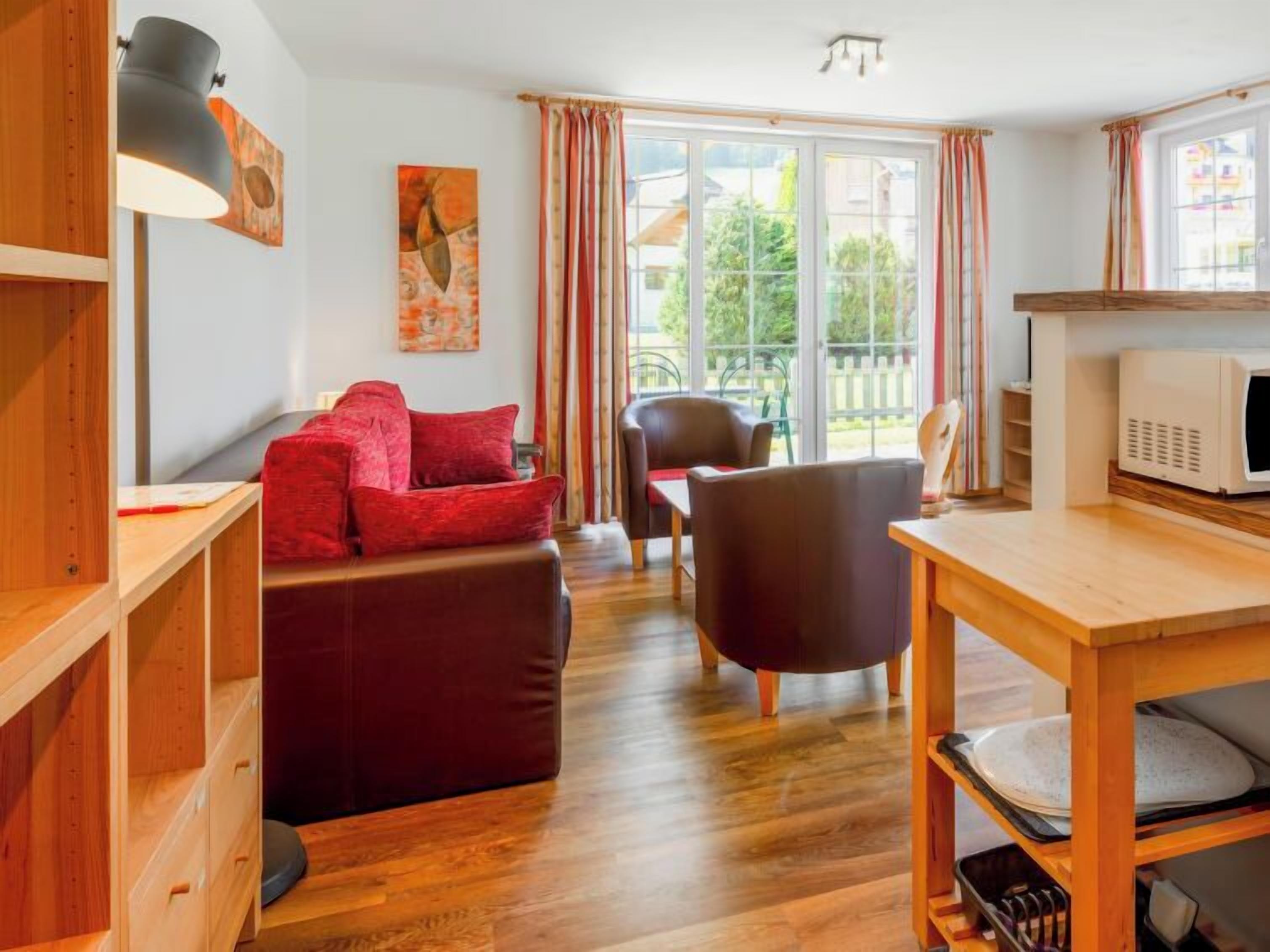 Een gezellige woonkamer met een rode bank, houten meubels, een eettafel en een groot raam met gordijnen.