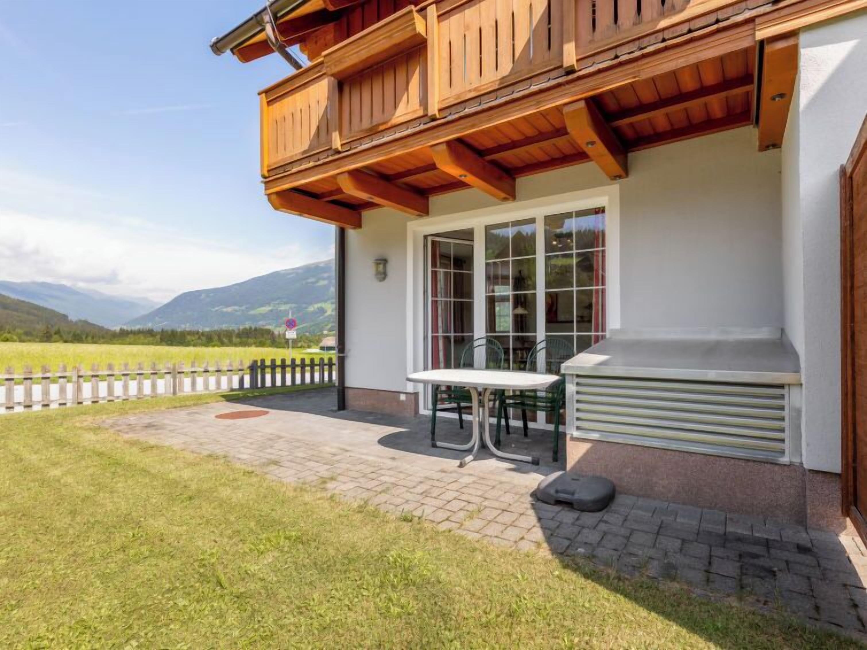 Ein Gebäude mit einem hölzernen Balkon, einem Tisch und Stühlen im Freien und Blick auf die Landschaft.
