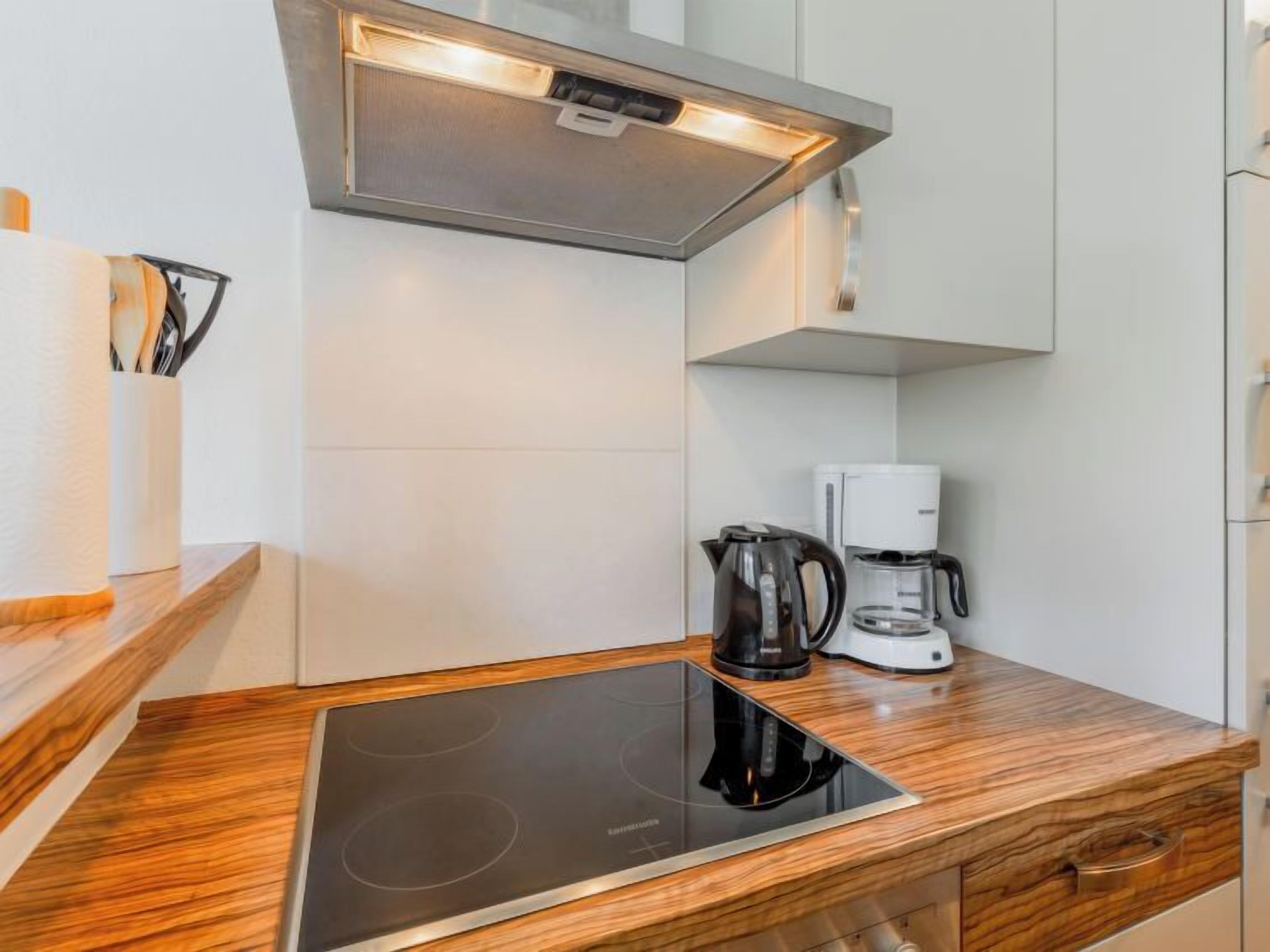 Een moderne keuken met een geïntegreerd inductiekookveld, een koffiezetapparaat en een waterkoker op een houten aanrecht.