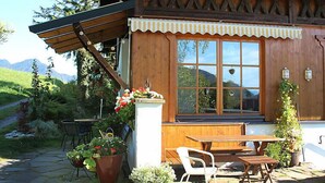 A wooden cabin with a stone patio, a wooden table, and chairs.