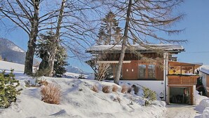 A snow-covered landscape with a chalet-style building, surrounded by trees and a mountain in the background.