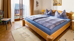 A bedroom with a wooden bed, two pillows, a nightstand, a lamp, a chair, a radiator, and a painting on the wall.