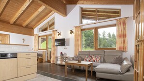 A spacious living area with a sofa, a coffee table, and a television. There is a kitchen with wooden cabinets and a dishwasher. Large windows provide natural light and views of the outdoors. - Ferienhof Sonnseitn by Interhome (Kaltenbach)