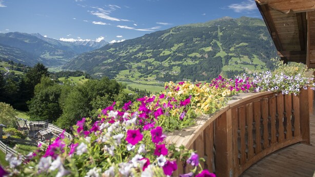 A wooden balcony with a view of a mountainous landscape and a garden with colorful flowers. - Ferienhof Sonnseitn by Interhome (Kaltenbach)