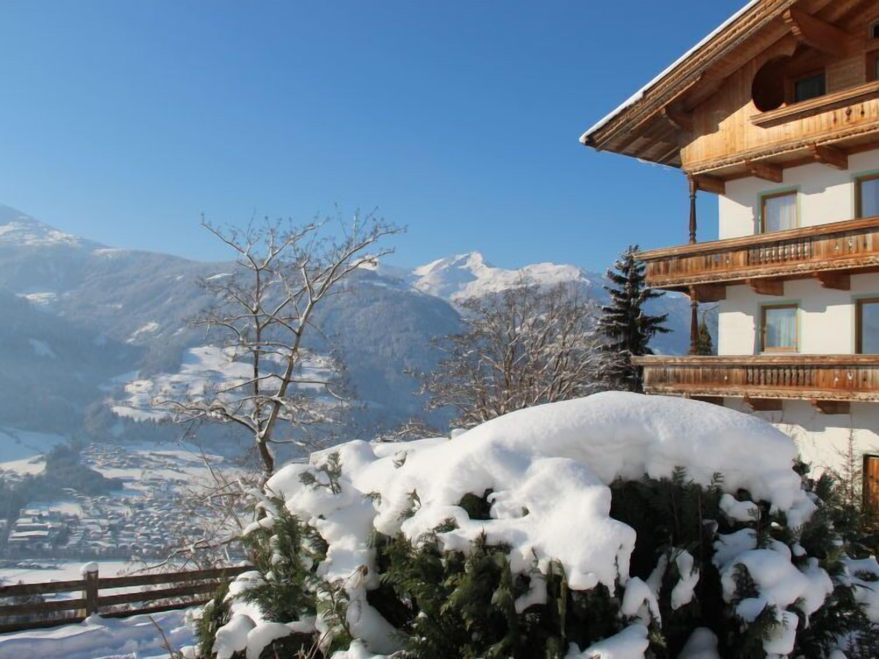 A mountain lodge with a wooden balcony and a view of snow-covered mountains.