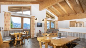 A cozy chalet with wooden beams, a dining area with a large table and benches, and a living area with a sofa and TV. - Ferienhof Sonnseitn by Interhome (Kaltenbach)