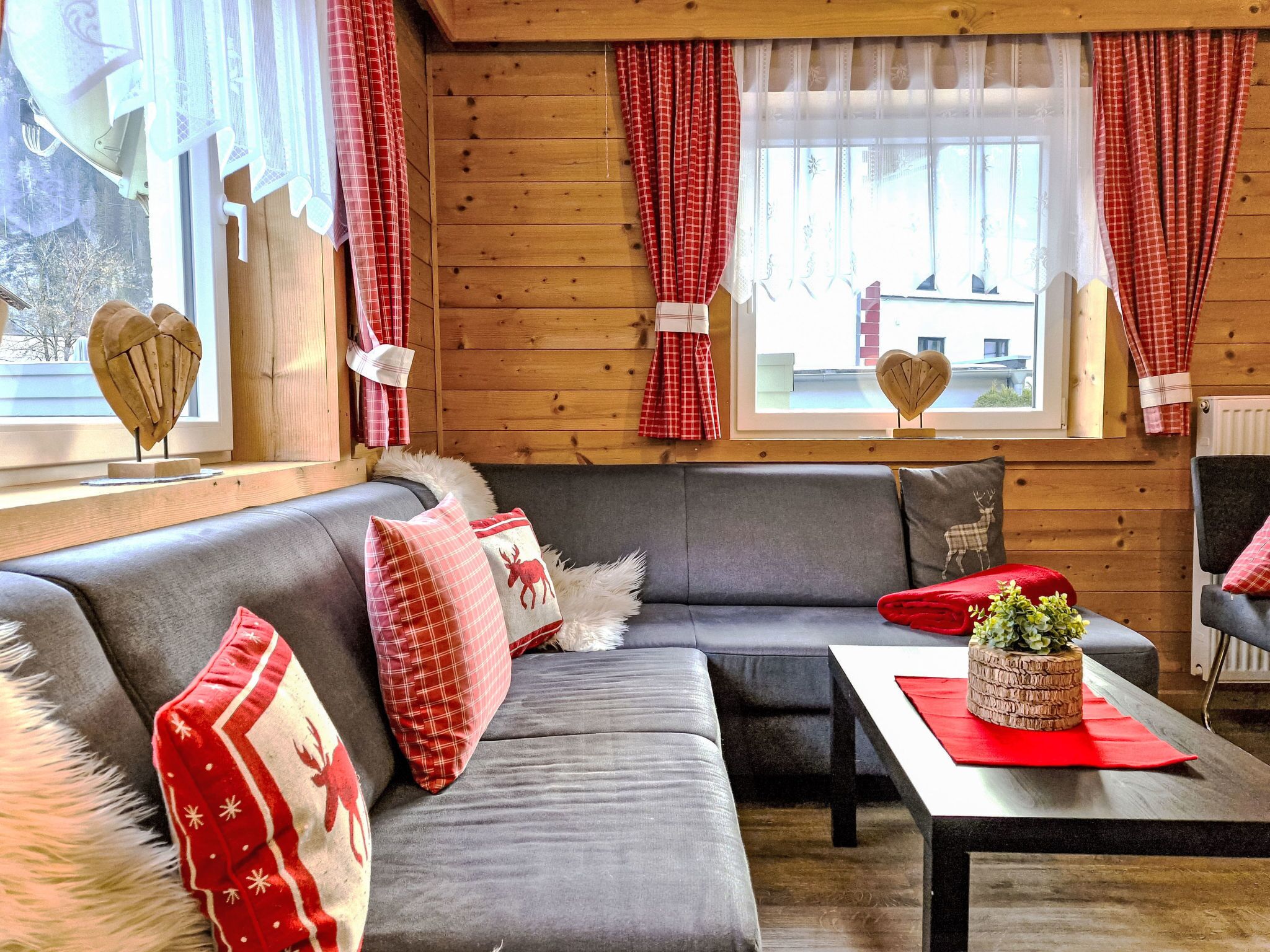 Ein gemütliches Zimmer mit einem grauen Sofa, roten und weißen Karottenvorhängen und einer herzförmigen Dekoration am Fensterbrett.