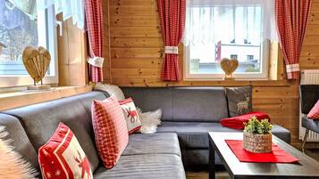 Ein gemütliches Zimmer mit einem grauen Sofa, roten und weißen Karottenvorhängen und einer herzförmigen Dekoration am Fensterbrett.