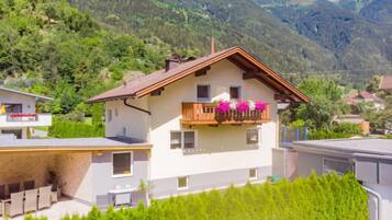 Eine zweistöckige Chalet mit Balkon, umgeben von üppiger Vegetation und Bergen.