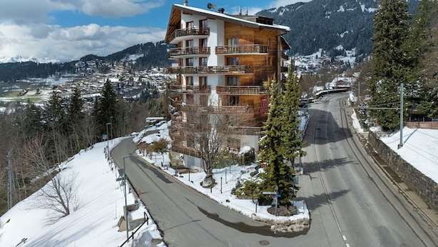 Un edificio a più piani con balconi, un paesaggio innevato e montagne sullo sfondo.