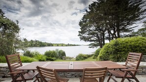 Ein Holztisch mit Stühlen steht auf einer Steinterrasse mit Blick auf einen See.