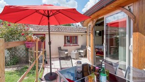 Un patio con sombrilla roja, mobiliario exterior y una mesa con bebidas.
