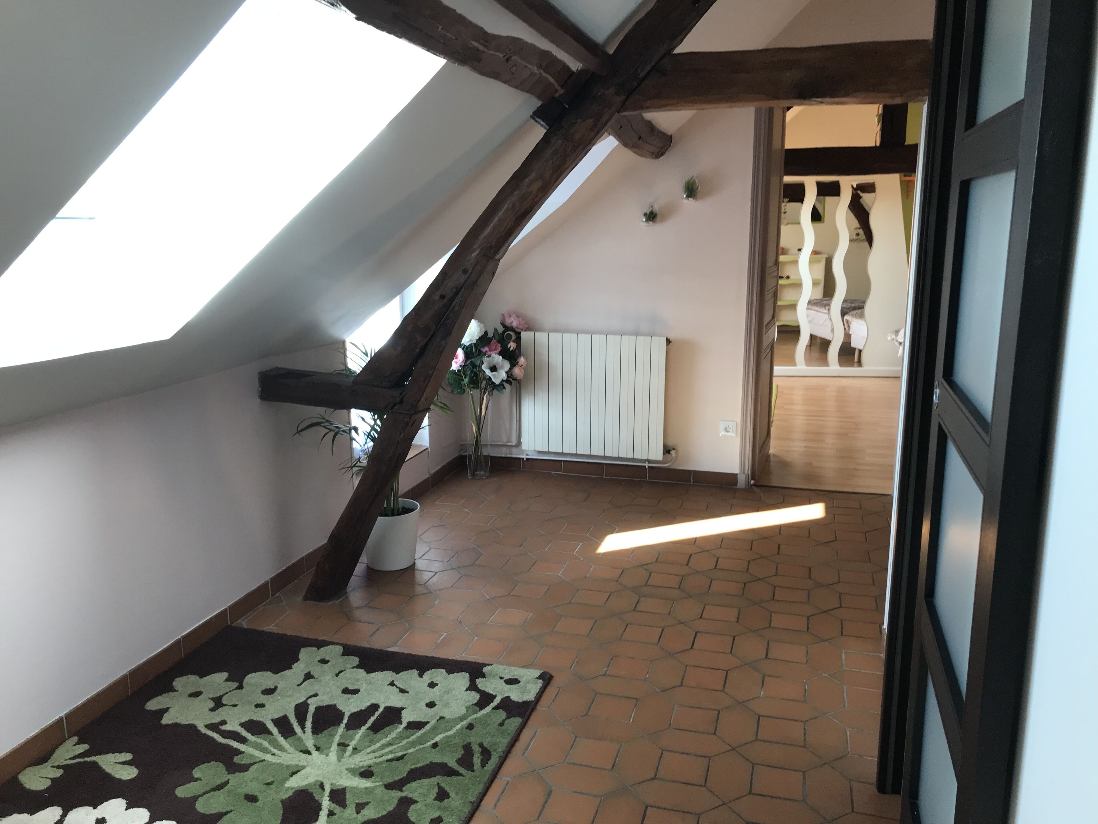 A room with a sloped ceiling, a radiator, a tiled floor, and a floral rug.