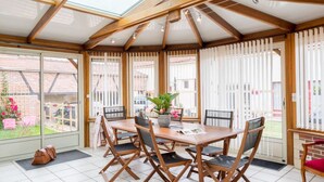 Un solárium con una mesa y sillas de madera, ventanas amplias y vistas a un jardín.