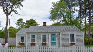 A small, single-story house with a white picket fence, a chimney, and a blue door.