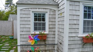 A house with white siding, a window with a white frame, and a pinwheel in the front yard.