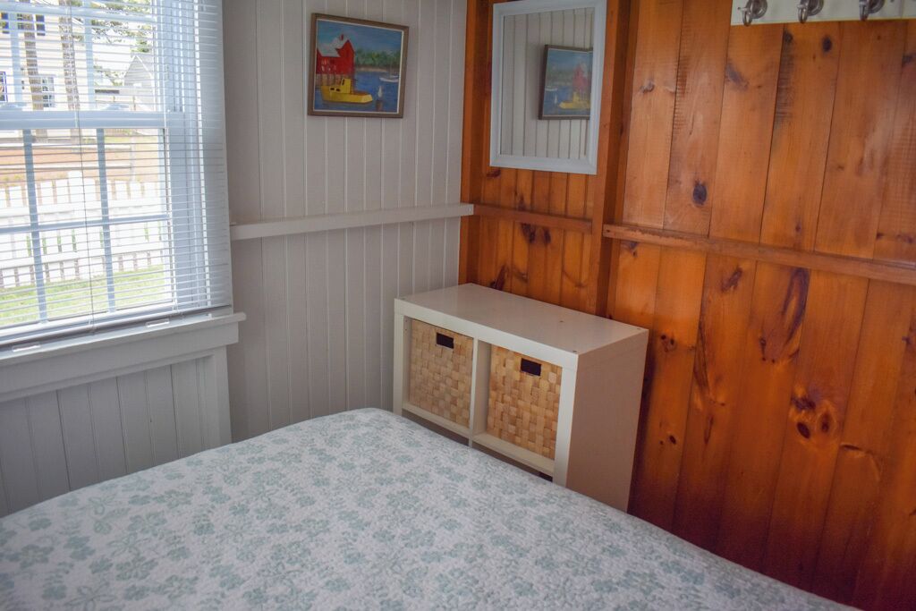 Une chambre à coucher avec un lit, des lambris en bois, une fenêtre avec des stores et deux petites armoires en bois.