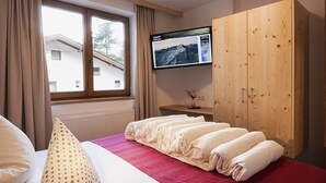 A hotel room with a bed, a wooden wardrobe, a television on the wall, and a window with curtains. - Falkner by Interhome (Längenfeld)