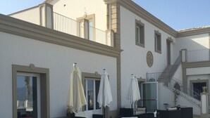 Un patio al aire libre con mobiliario y sombrillas, una escalera y la fachada de un edificio.