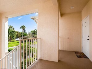 A balcony with a white railing, beige walls, and a door to the right.