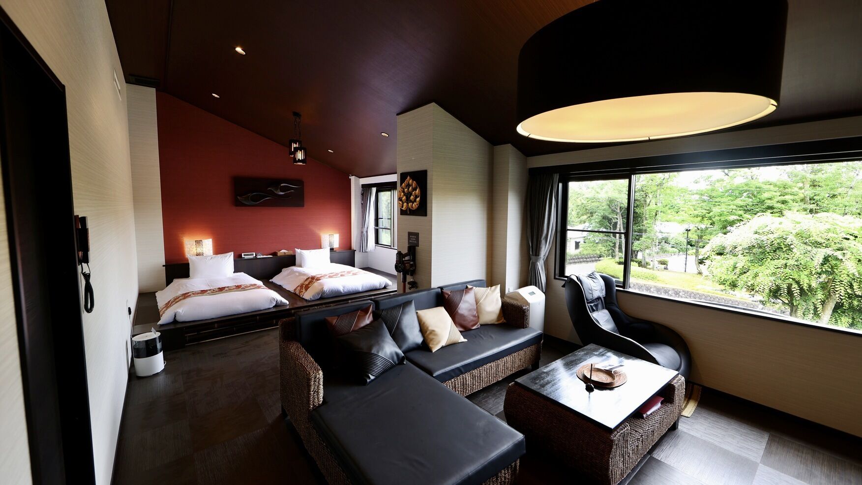 Habitación de hotel moderna con sofá, sillón, cama y un amplio ventanal con vistas a zonas verdes.