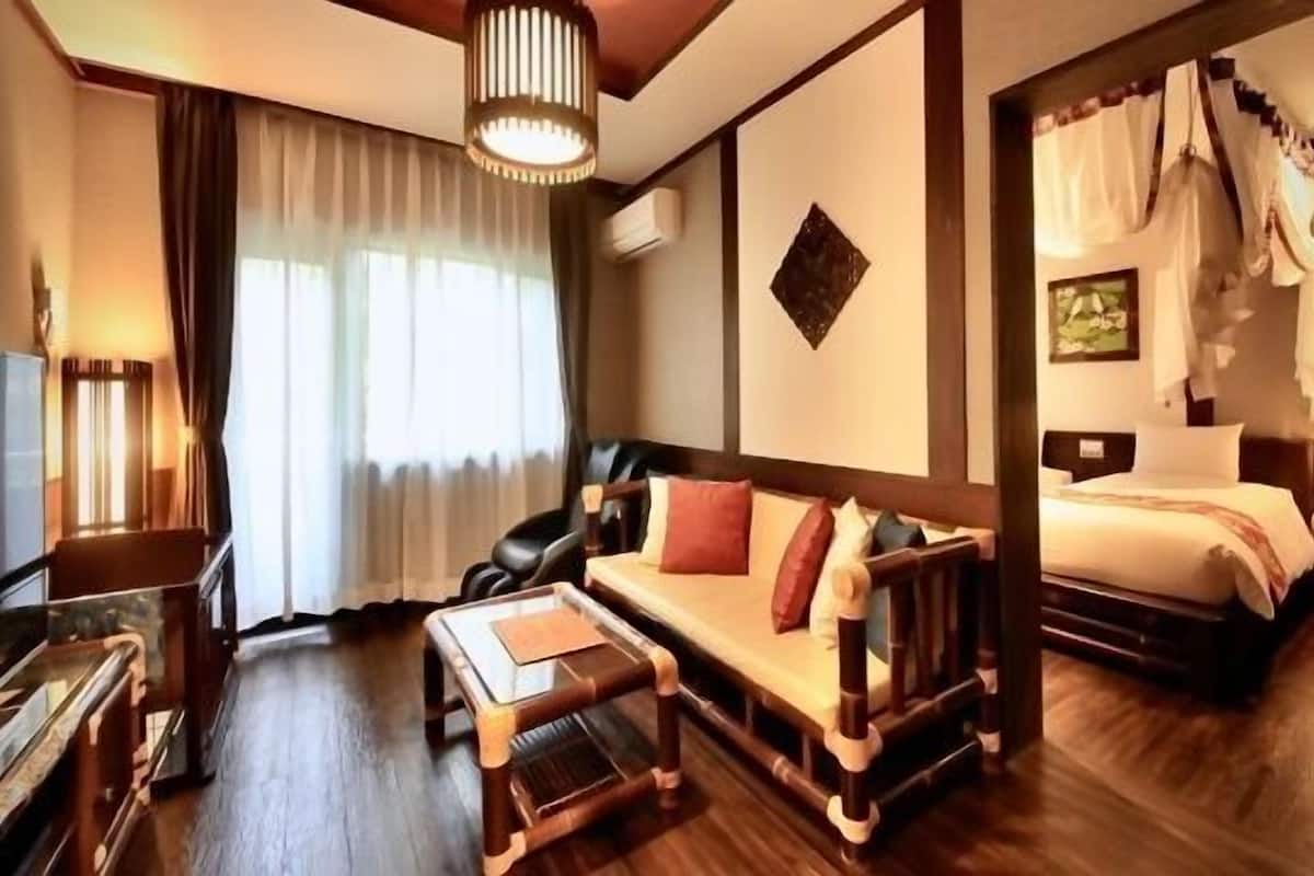 A hotel room with a sofa, a bed, a wooden bench, a piano, and a large window with curtains.