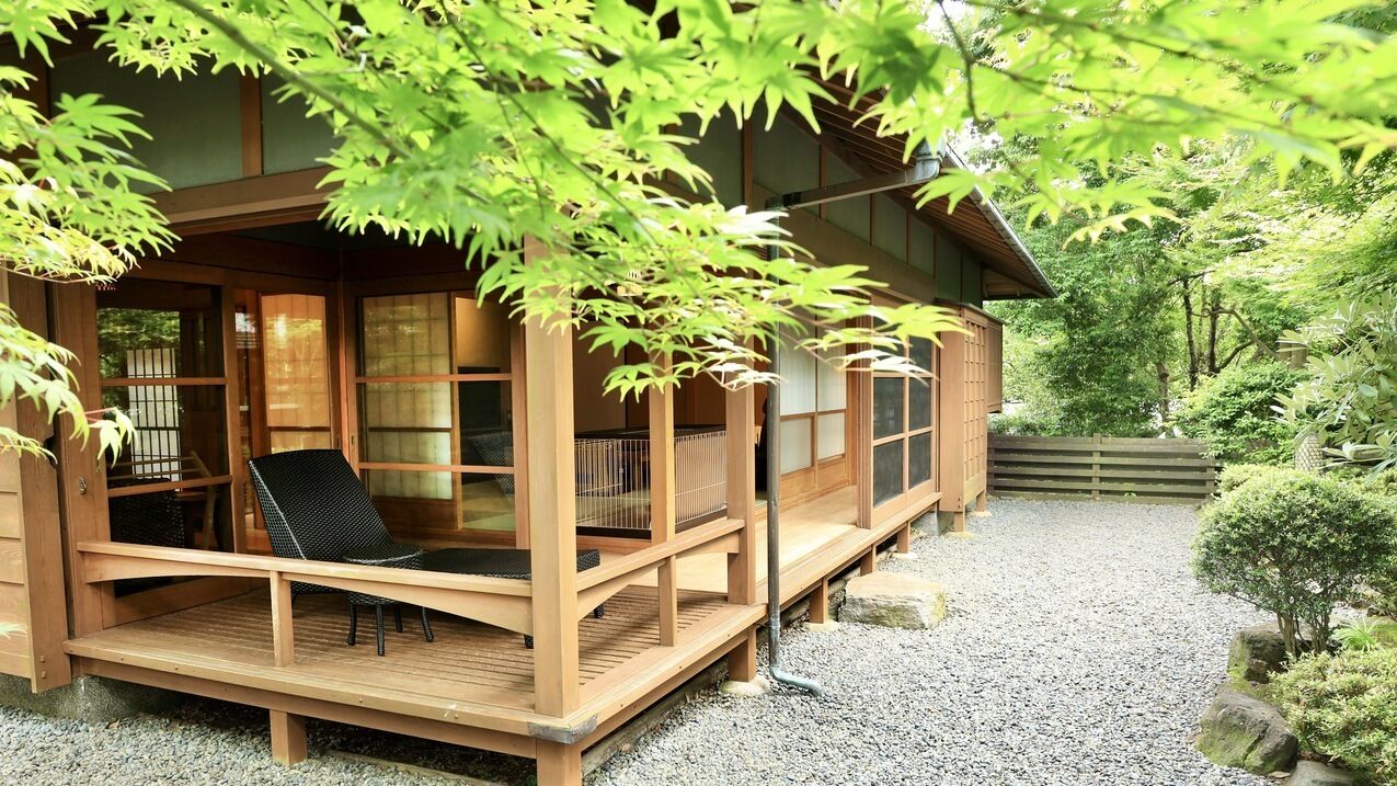 Una casa tradicional japonesa de madera con un porche de madera, una silla y un sendero de grava.