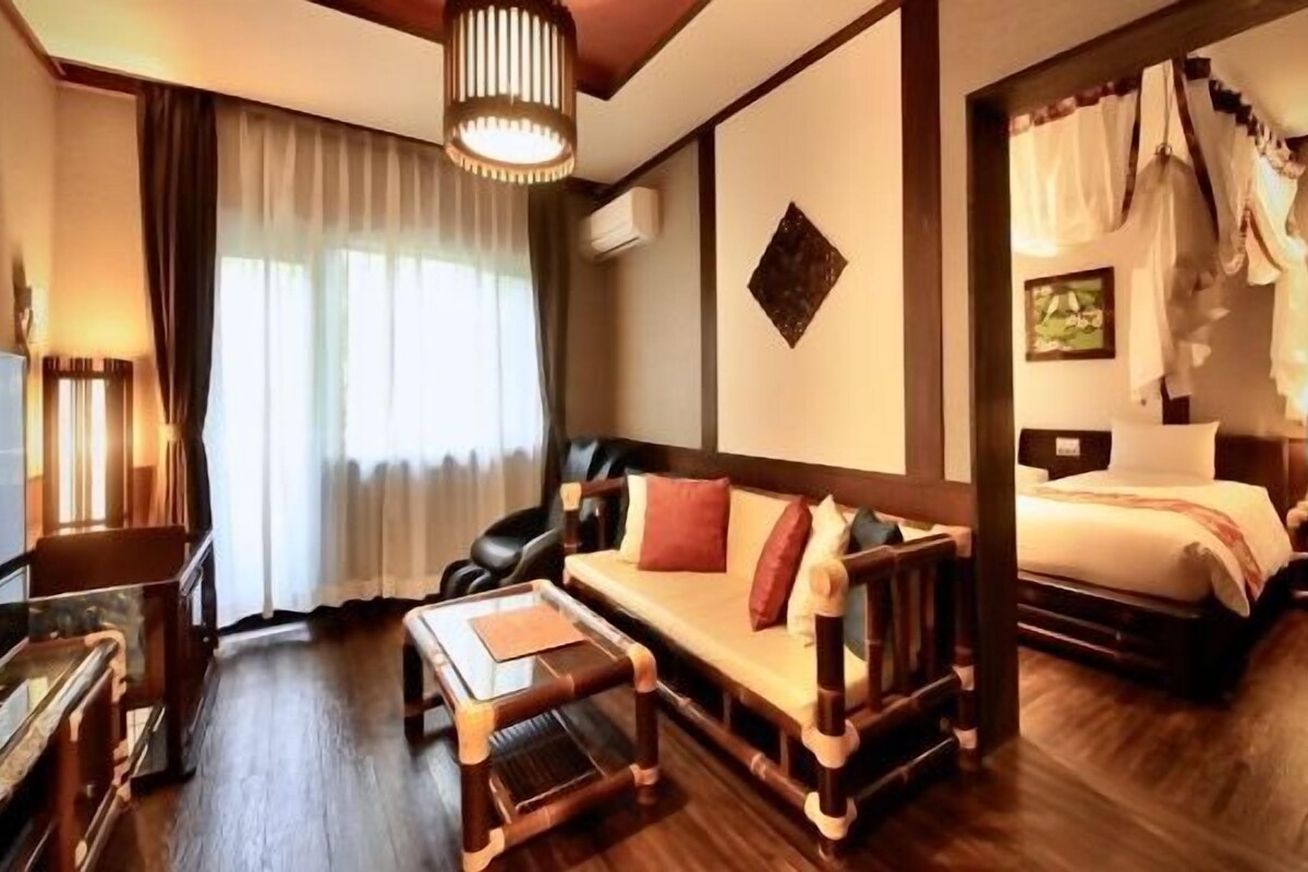 A hotel room with a sofa, a bed, a wooden bench, a piano, and a large window with curtains.