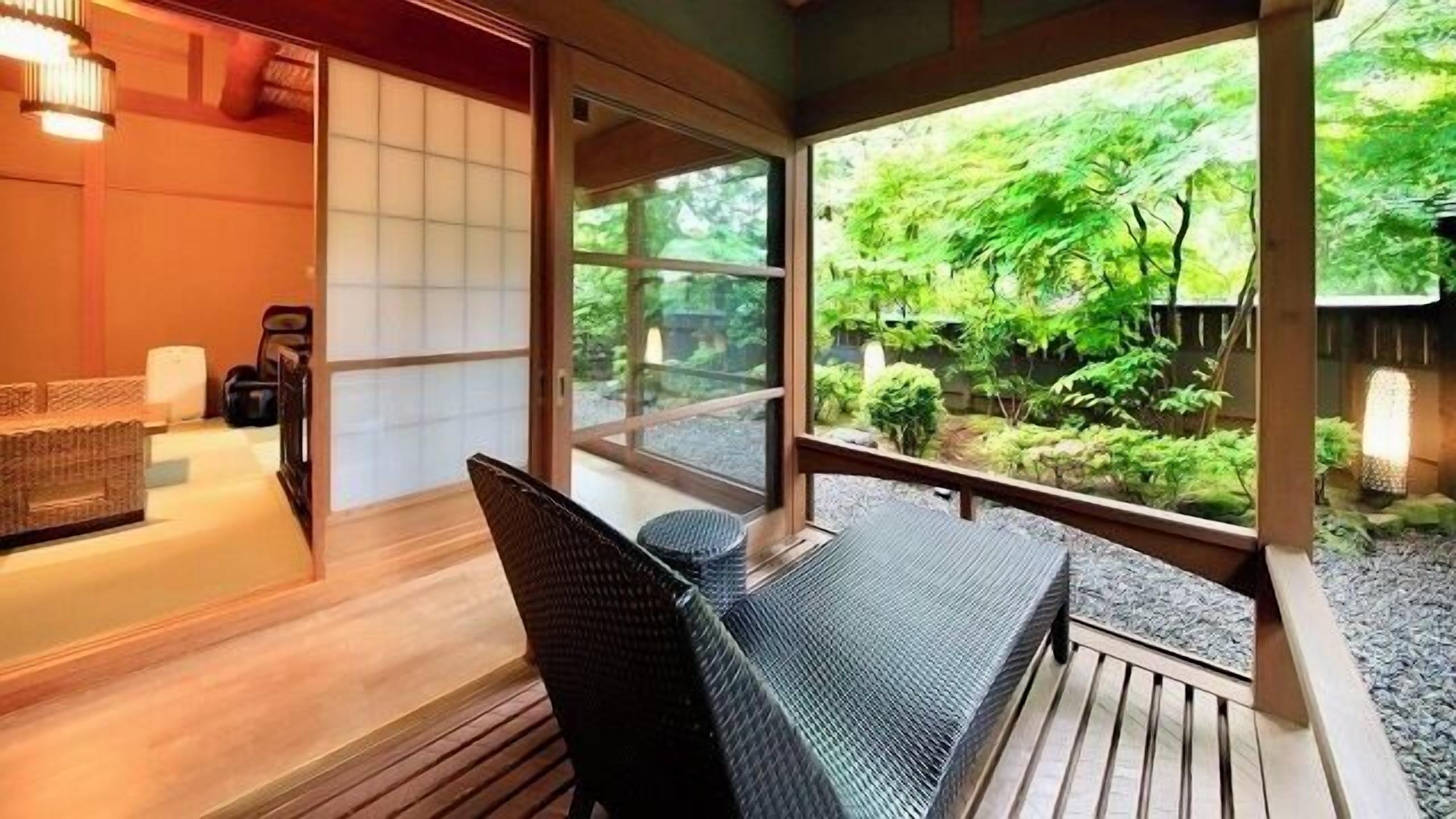 Una habitación con piso de madera, una silla, una mesita y vista a un jardín por un ventanal amplio.