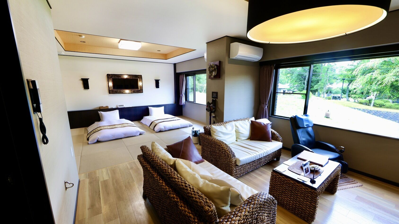 Habitación moderna con cama, dos sofás, una mesita de centro y un gran ventanal con vistas a la vegetación.