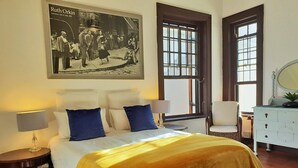 A bedroom with a bed, two bedside tables, a chair, a dresser, and a large window. - Westbank (Cape Town)