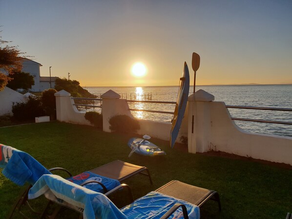 A patio with a view of the sunset over the sea, a kayak, and lounge chairs. - Westbank (Cape Town)